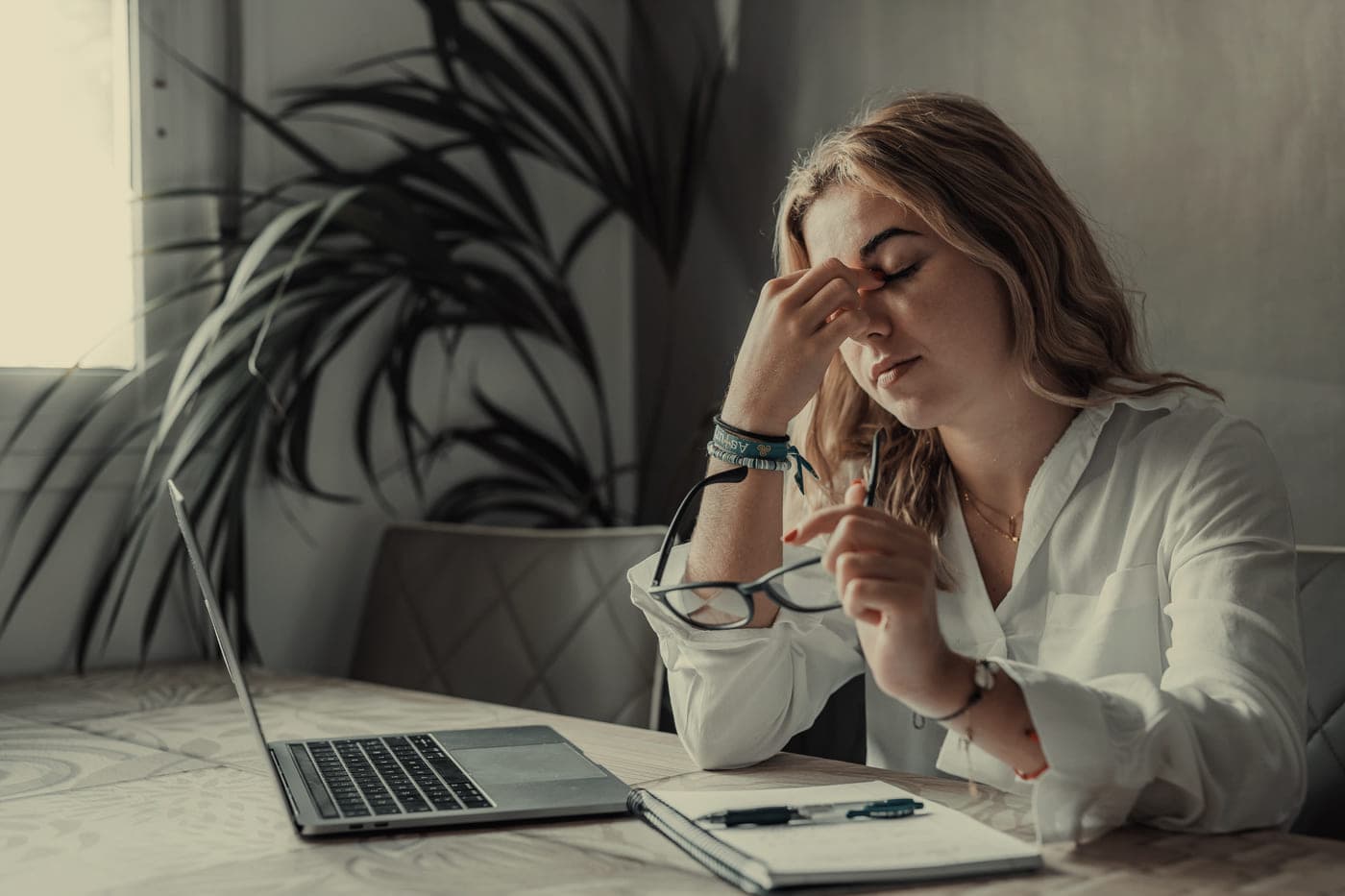 A woman at a laptop with her eyes closed, pinching the bridge of her nose